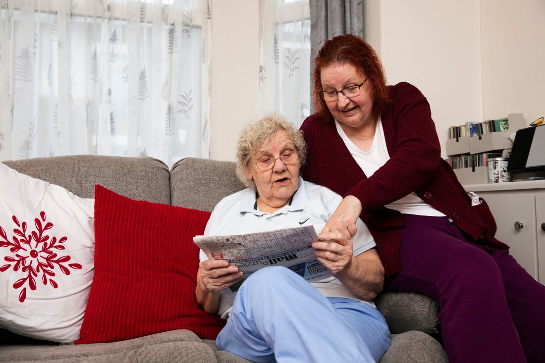 Two women sitting on a couch looking at a newspaper.