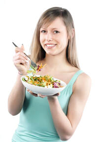 Woman looking at camera while eating salad with a fork