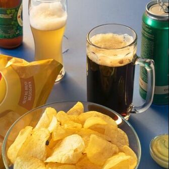 Store bought potato chips in glass bowl, glass of beer and glass of soda.