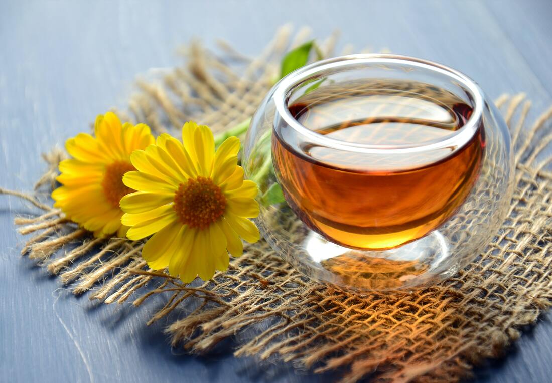 Small glass of honey on table with two yellow fowers beside it.