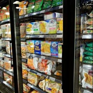 Looking through glass refrigerator doors at grocery store frozen boxed food section.