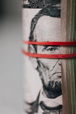 Banded roll of thick currency with Abraham Lincoln looking at the viewer.