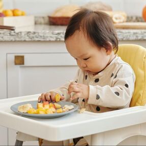 Small child in highchair eating fruit off of a place.